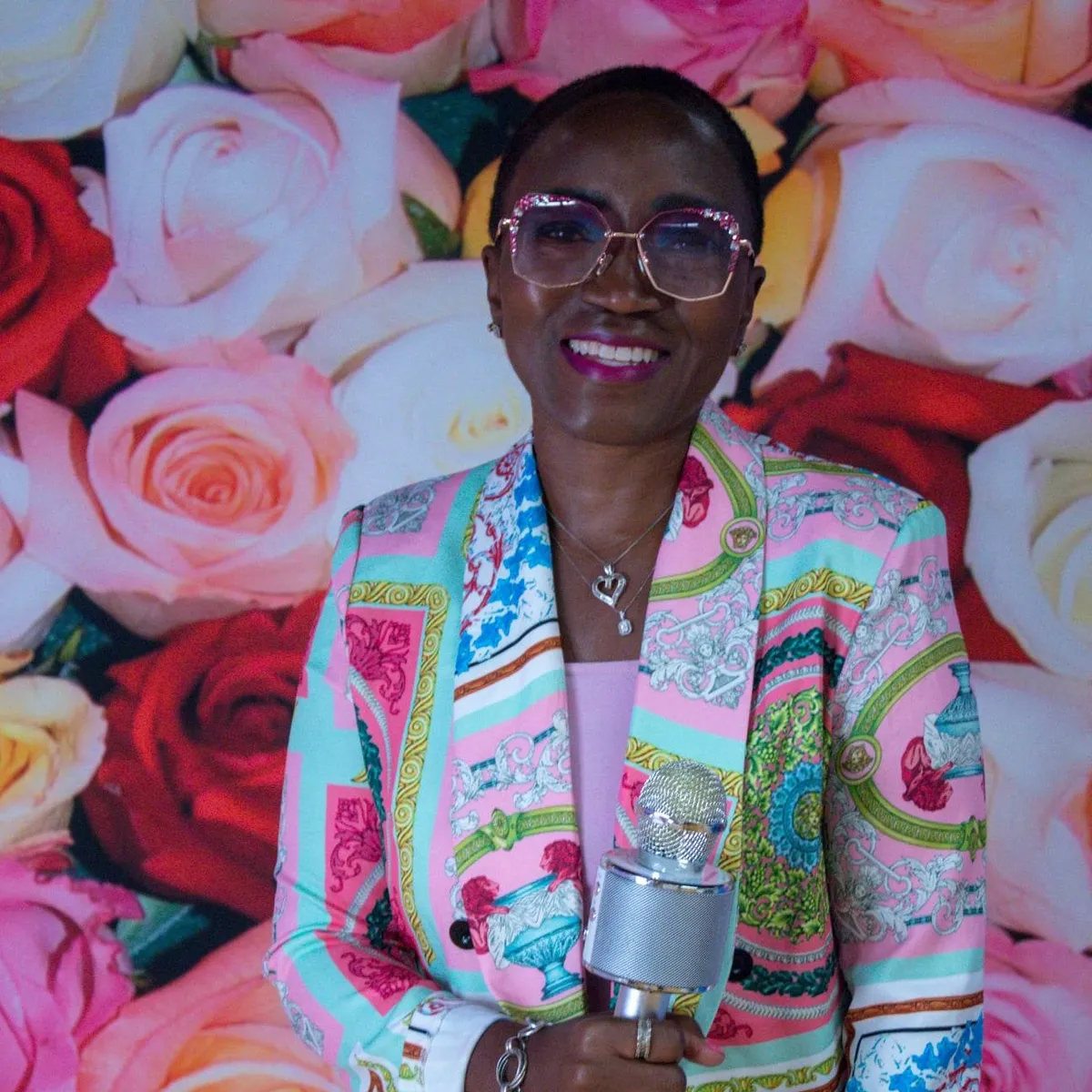 Charise smiling with mic in front of a wall of roses